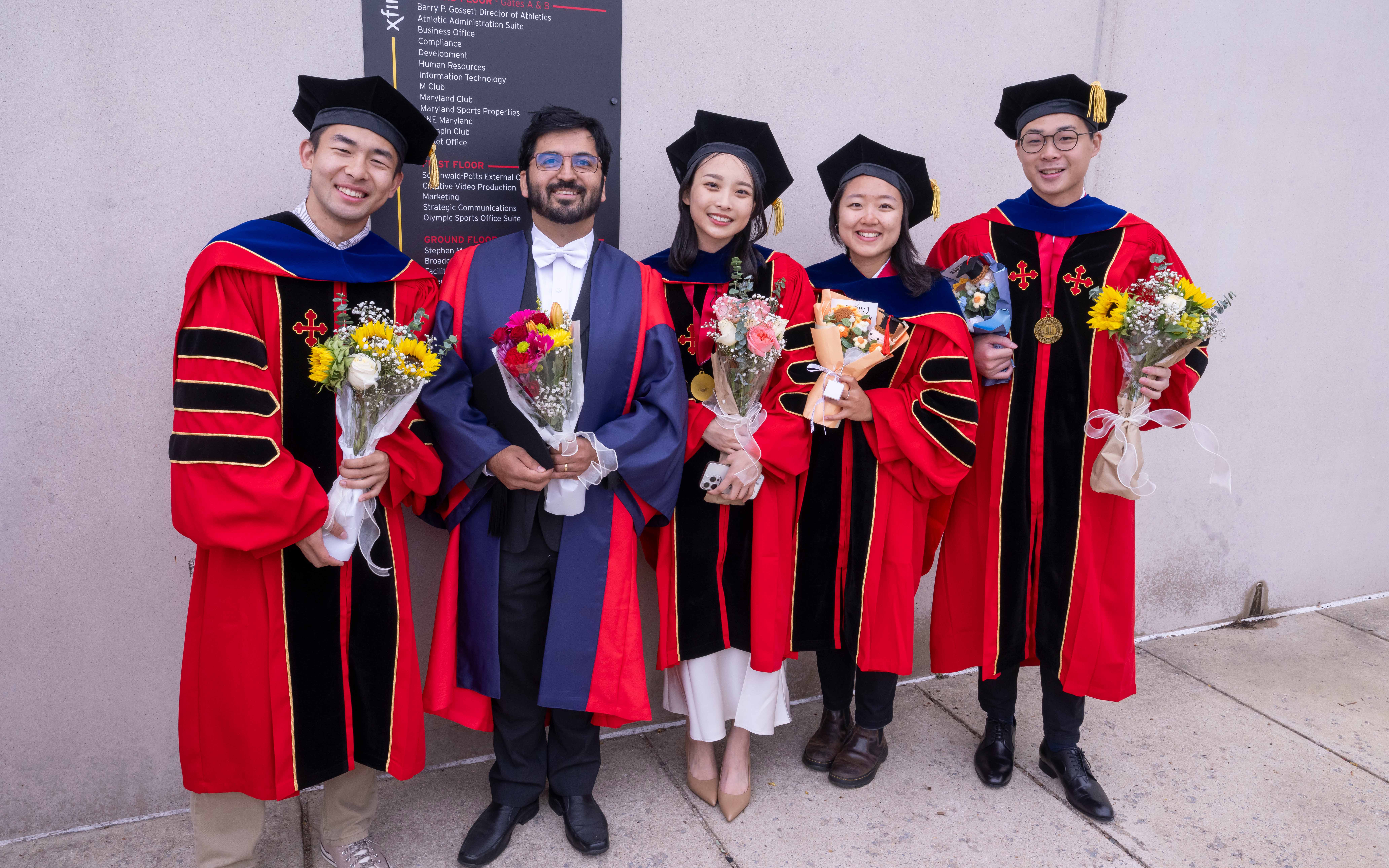Students wearing graduation regalia standing with professor.