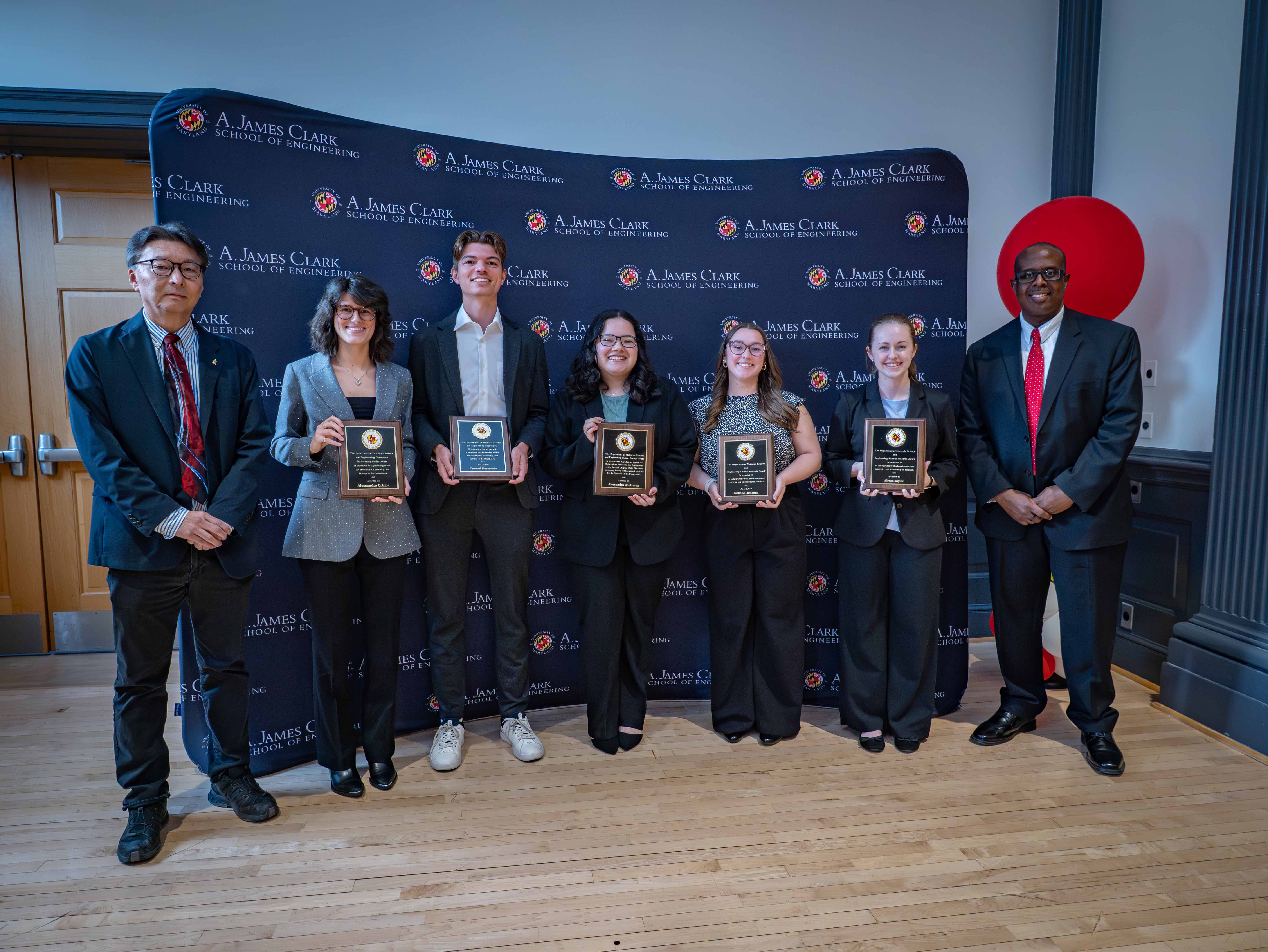 Students and professor standing together holding awards.