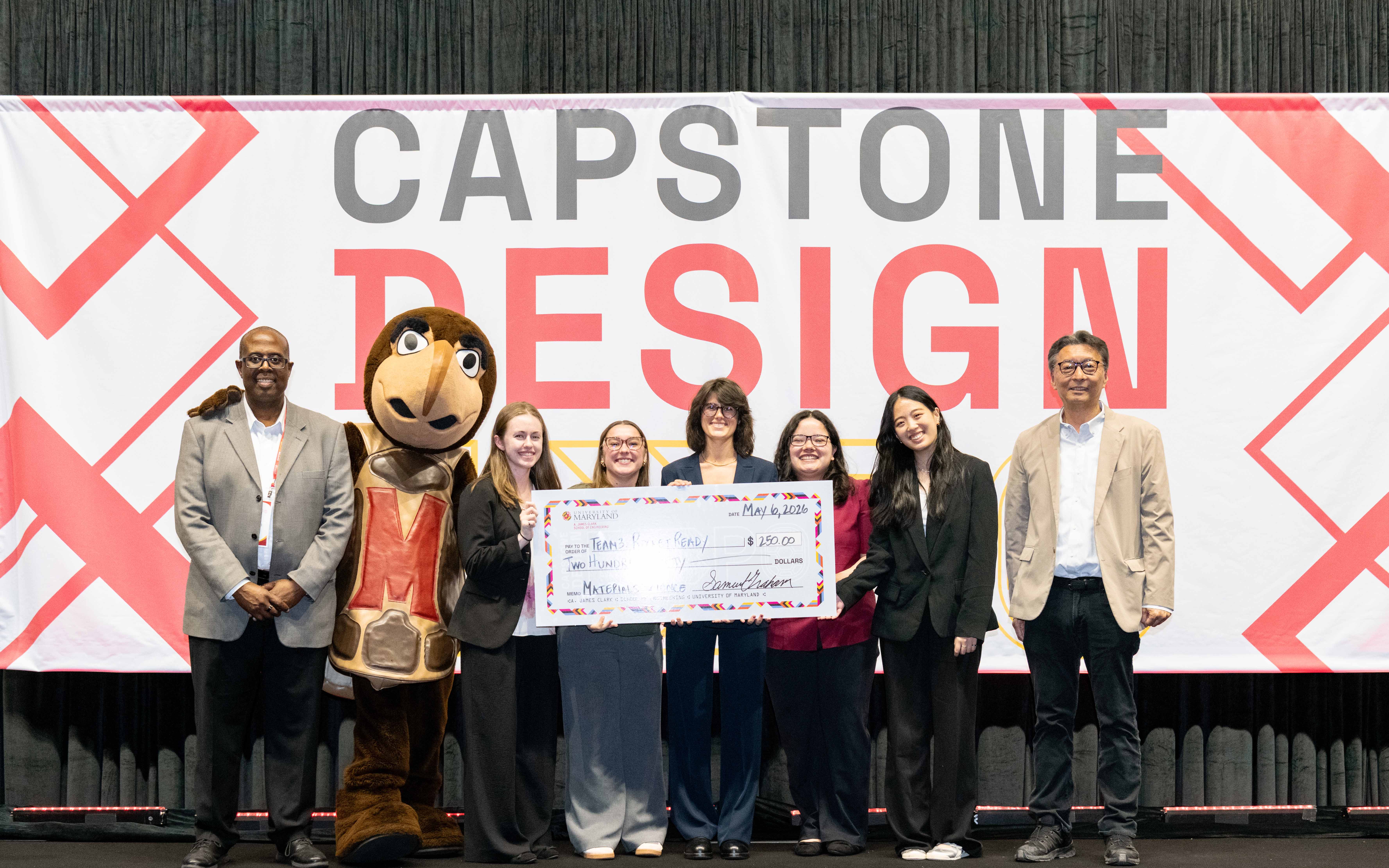 Group of seven individuals and the university mascot, with five in the center holding a large check.